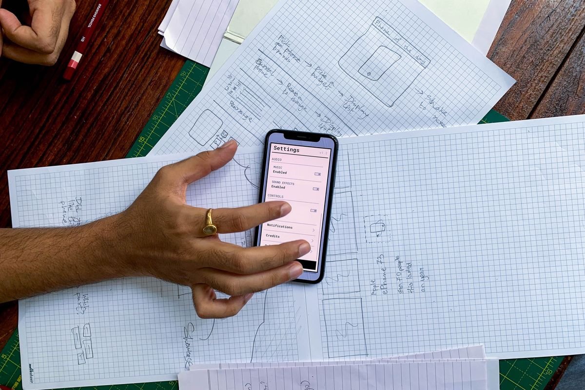 Main tenant un smartphone au-dessus de croquis de maquettes d'application