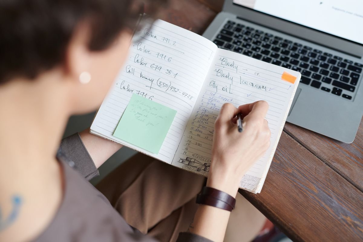 Personne prenant des notes dans un carnet à côté d'un ordinateur portable