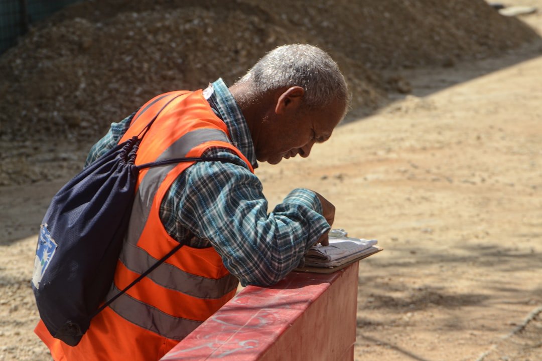 Artisan du bâtiment en gilet de sécurité orange rédigeant un document sur un chantier